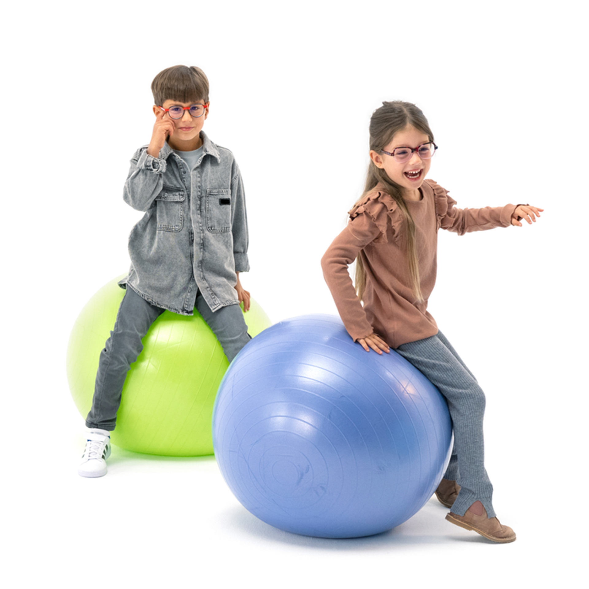 Хлопчик і дівчинка в окулярах граються, підстрибуючи на гімнастичних м&apos;ячах.